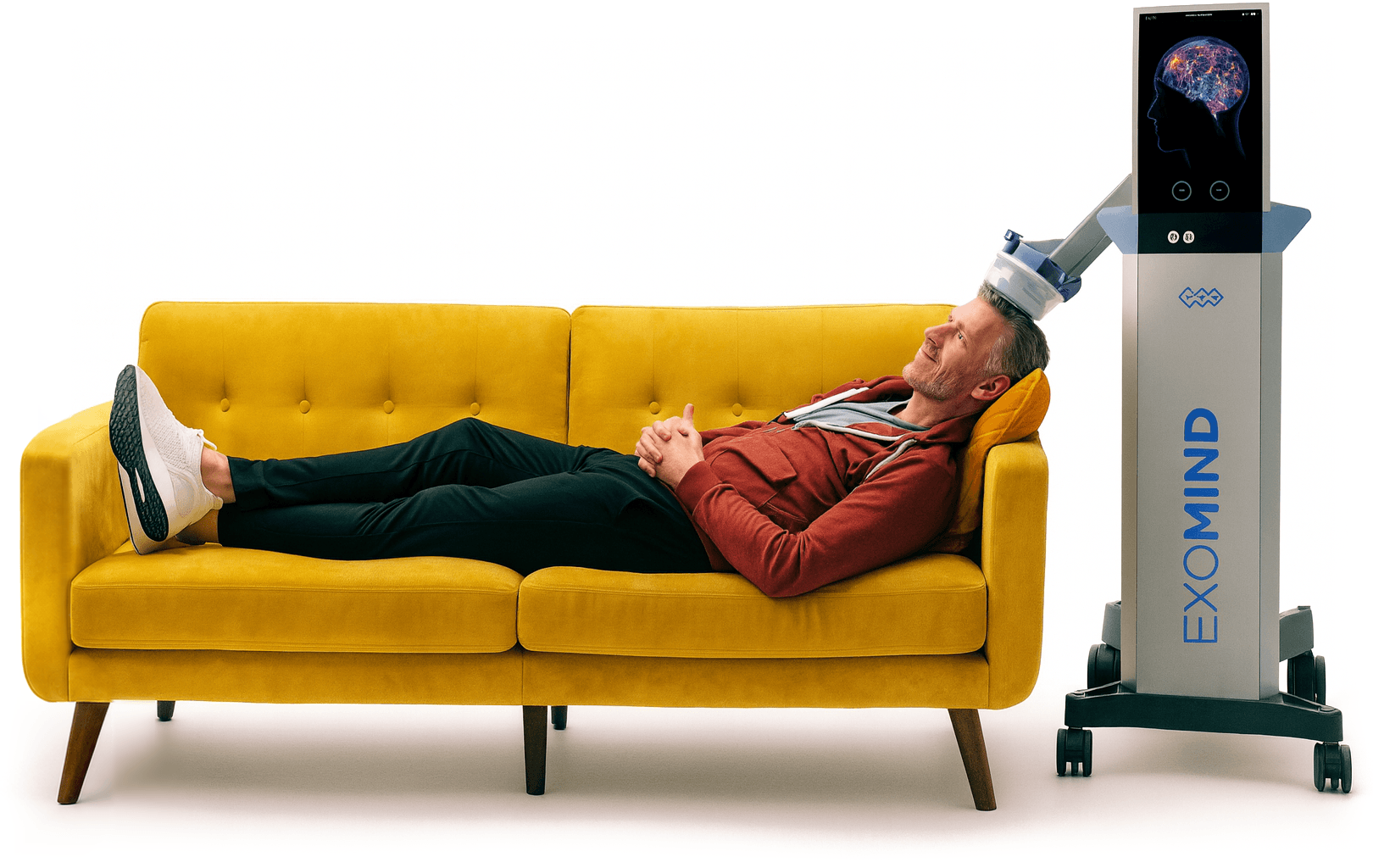 A person reclining on a sofa receiving Exomind treatment, with the Exomind unit positioned at their head.